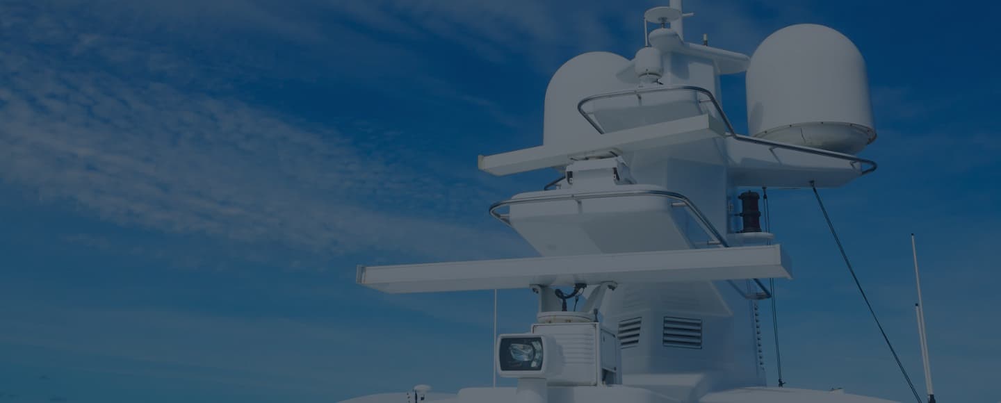 Maritime navigation and radar equipment against a clear blue sky with scattered clouds. The equipment is painted white, mounted on the top of a ship, and includes various antennae, radar domes, and communication devices