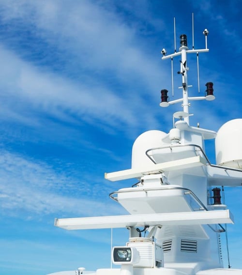 Close-up of a ship's communication and navigation mast against a clear blue sky, featuring various antennas, radars, and navigation lights, indicative of modern maritime equipment.